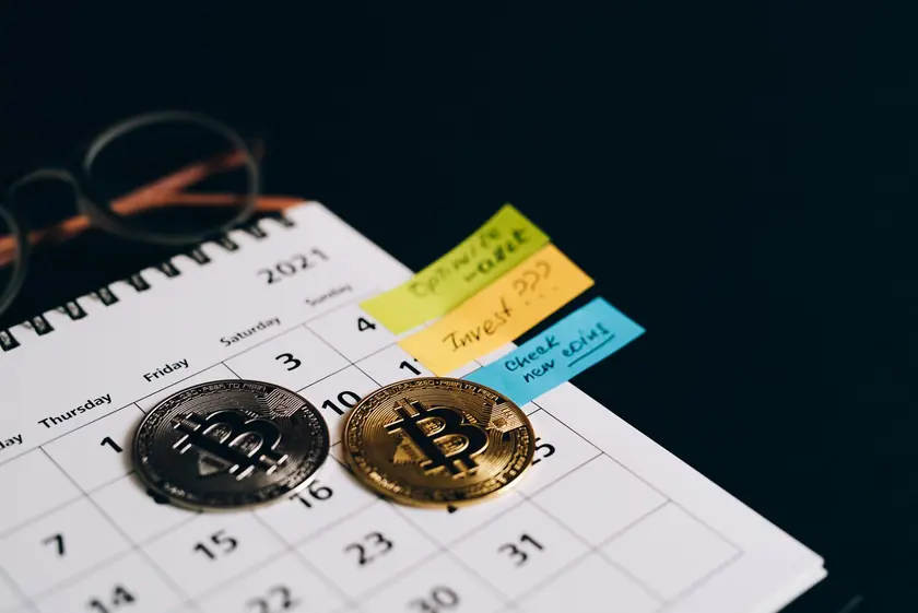 Monedas de Bitcoin colocadas en un calendario con notas adhesivas para planificación de inversiones.