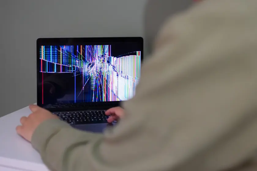 A person interacts with a laptop that has a cracked and distorted screen.