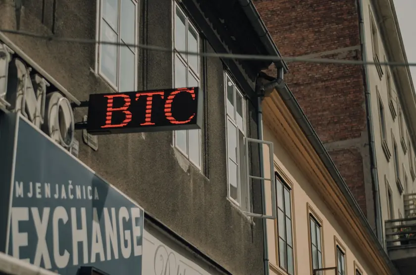 Fachada de un edificio con un letrero destacado de BTC y una casa de cambio, indicando una ubicación de criptomonedas.