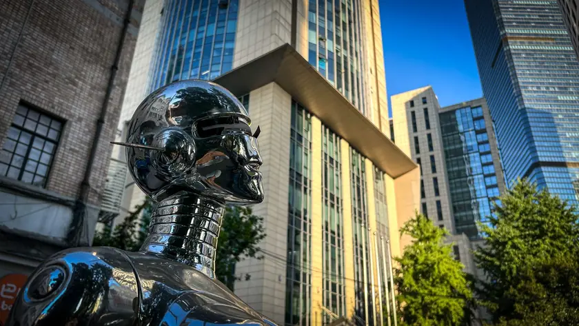 現代的な高層ビルの前にあるロボット彫刻、未来都市を形作る技術を示しています。